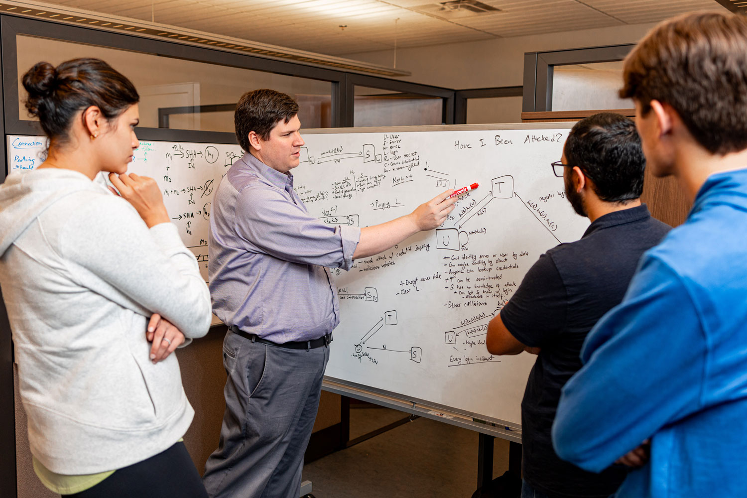 Scott Ruoti works on white board with grad students in lab
